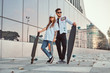 © Fxquadro - Attractive young couple dressed in trendy clothes posing with skateboards near skyscraper.
