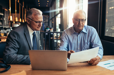 Wall Mural - Senior businessmen at cafe discussing over a report