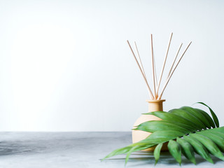 aroma reed diffuser home fragrance with rattan sticks on a light background with palm leaves and shadows.