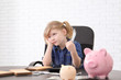Cute little girl with money and piggy banks at table indoors