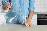 Fototapeta Łazienka - Woman pouring water into glass at table, closeup