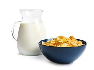 Bowl with crispy cornflakes and jug of milk on white background