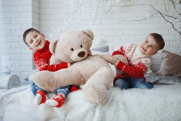 Wall Mural - Two brothers Boy in a Christmas red sweater with a picture of a deer sitting on a bed with pillows.