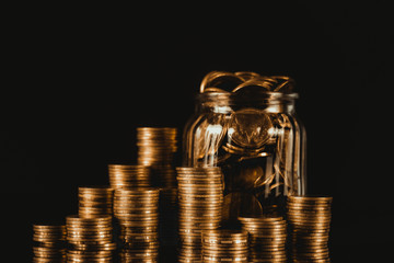 Coins stacks and gold coin money in the glass jar on dark background, for saving for the future banking finance concept.