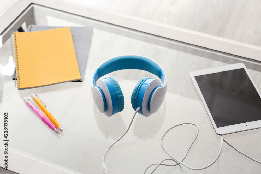 Headphones with tablet PC and stationery on glass table
