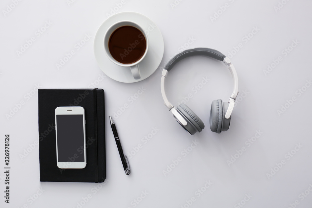 Headphones with mobile phone and cup of coffee on white table