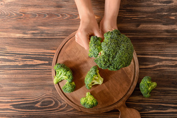 Female hands with fresh broccoli on wooden background