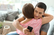 Young cheater texting lover while hugging his girlfriend at home