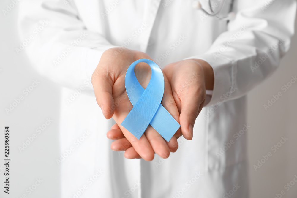 Female doctor holding blue ribbon, closeup. Cancer awareness concept