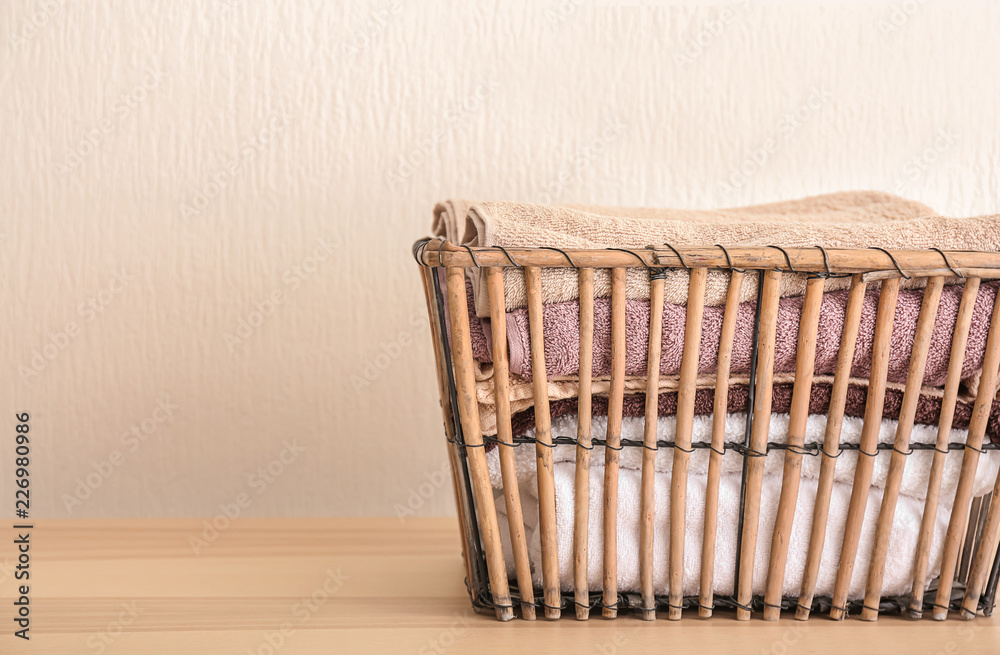 Laundry basket with clean towels on table near white wall