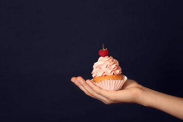 Female hand holding delicious cupcake on dark background