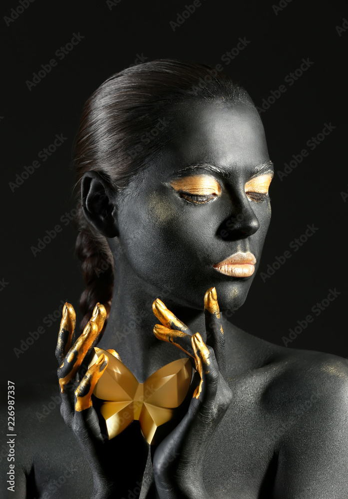 Beautiful woman with black and golden paint on her body against dark background - obrazy, fototapety, plakaty 