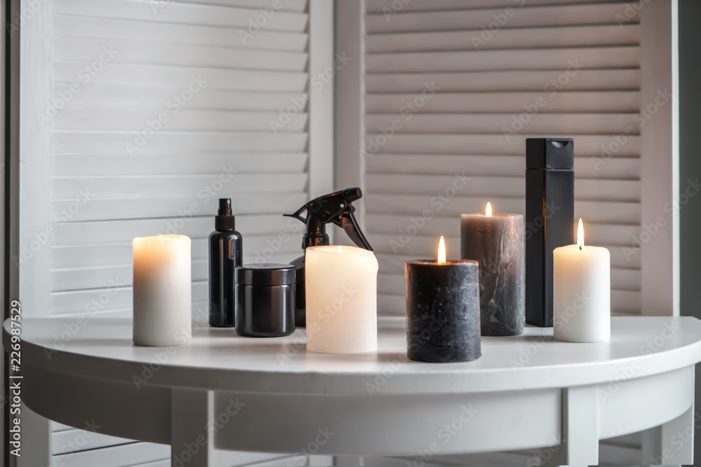Burning candles with cosmetics on white table indoors