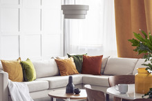 Lamp Above Table In Bright Living Room Interior With Yellow Pillows On White Corner Sofa. Real Photo