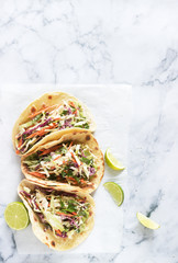 Tacos with guacamole and coleslaw served with lime slices on a light background.