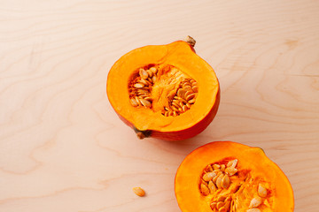 Two halves of raw pumpkin with seeds on wooden background