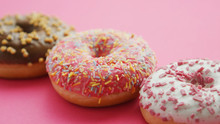 Closeup Of Few Sweet Doughnuts With Colorful Glaze And Sprinkles Composed In Row On Bright Pink Surface