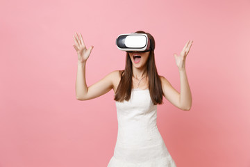 Portrait of excited bride woman in white wedding dress, headset of virtual reality spreading hands isolated on pastel pink background. Organization of wedding concept. Copy space for advertisement.