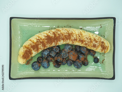 Fotografía Postre de plátano con arándanos y cacao puro en polvo.
