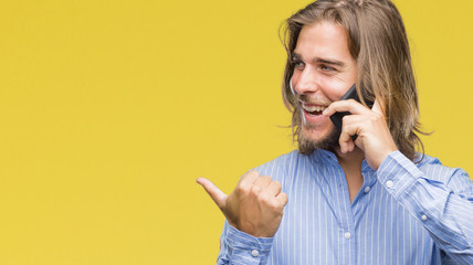 Poster - Young handsome man with long hair over isolated background talking on the phone pointing and showing with thumb up to the side with happy face smiling