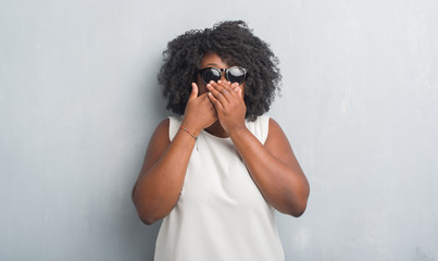 Sticker - Young african american plus size woman over grey grunge wall wearing fashion sunglasses shocked covering mouth with hands for mistake. Secret concept.