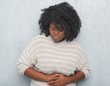 © Krakenimages.com - Young african american plus size woman over grey grunge wall wearing a sweater with hand on stomach because indigestion, painful illness feeling unwell. Ache concept.