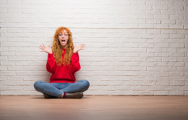 Poster - Young redhead woman sitting over brick wall celebrating crazy and amazed for success with arms raised and open eyes screaming excited. Winner concept