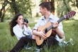 © soleg - young couple sitting in the forest and playing guitar, taking photo on old camera, summer nature, bright sunlight, shadows and green leaves, romantic feelings