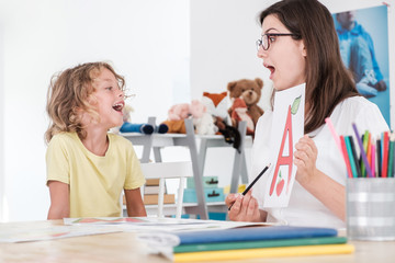 Wall Mural - A happy child pronouncing a letter during speech therapy with a specialist.