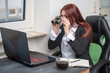 © Auslander - young professional woman sitting in the office in front of a laptop, looking at through binoculars, she is focused, looking for something