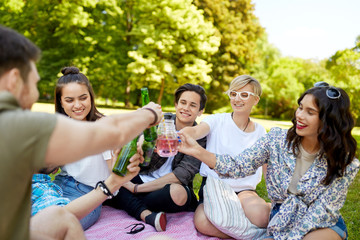 Canvas Print - leisure, people and celebration concept - happy friends clinking non alcoholic drinks at picnic in summer park