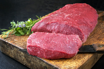 Wall Mural - Raw roast beef with herbs offered as closeup on an old rustic wooden cutting board