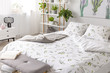 Green plant pattern on white bedding and pillows on a bed in a nature loving bedroom interior. Real photo.