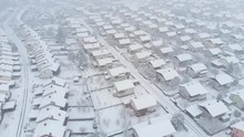 AERIAL: Pristine White Snow Covers The Empty Streets Of An Idyllic Suburban Neighborhood. Flying High Above The Rooftops Of Houses In The Tranquil Village On A Snowy Day. Blizzard In The Suburbs.