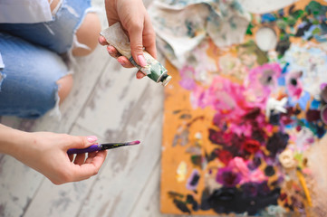 Young female student having classes at art studio, trying to mix different watercolors on cardboard.