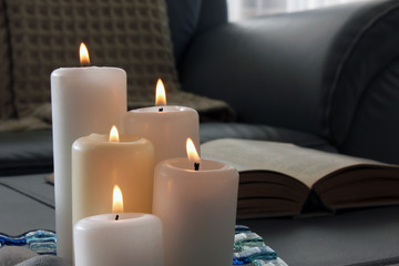 Wall Mural - Burning candles, pebbles, glass tray, open book in gray sofa with blanket background. Interior decoration, living room.