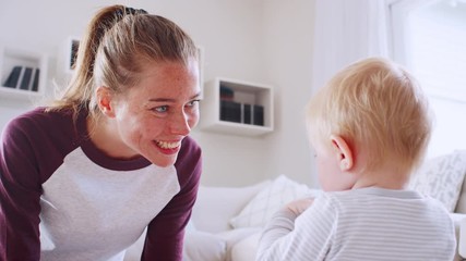 Wall Mural - Young mother making a face to toddler son at home