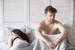Young millennial attractive couple lying in bed under blanket at home. Woman sleeping, depressed and frustrated man thinking about relationships. Family have problems in sexual life impotence concept