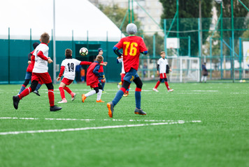 Wall Mural - football teams - boys in red, blue, white uniform play soccer on the green field. boys dribbling. dribbling skills. Team game, training, active lifestyle, hobby, sport for kids concept