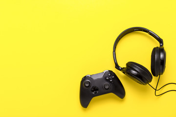 Wall Mural - Black headphones and a gamepad on yellow background. Concept of the game on the console or computer. Rest after work. Cybersport. Flat lay, top view