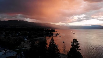 aerial drone shot flying over lake alongside lakefront houses with orange and blue colourful sky at 