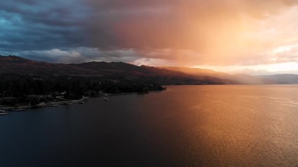 aerial drone shot flying over lake towards rain and mountains with orange and blue colourful sky at 