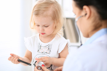 Wall Mural - Doctor and patient baby in hospital. Little girl is being examined by pediatrician with stethoscope. Health care, insurance and help concept