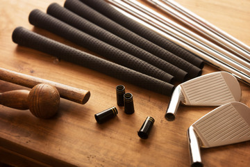 Golf club making. Golf club components on a work desk or work bench. grips, shaft, ferrules and, iron head.Focus is on black ferrule parts. Shallow depth of field.