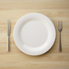 Fototapete - Top view of ceramic plate with fork and knife on wooden table. 3d rendering