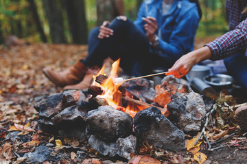 Two young girls girlfriends roasting sweet marshmallow on a fire in the evening in the autumn forest.