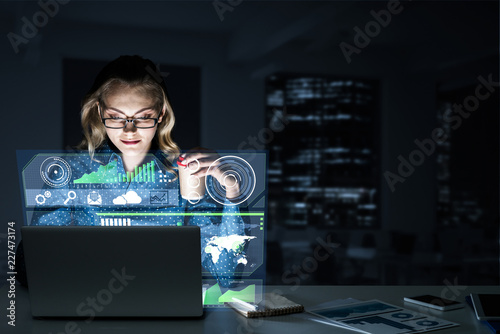 Fotografía Beautiful blonde working on laptop and infographs out of screen.