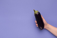 Female Hand Holding Fresh Eggplant On Purple Background
