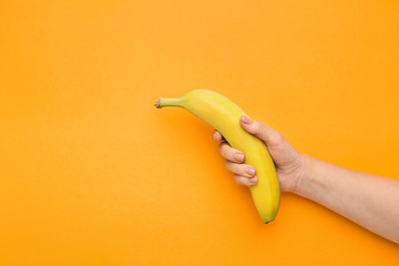 Female hand holding banana on orange background