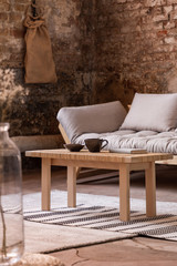 Wall Mural - Wooden table on rug in front of grey settee in industrial interior with brick wall. Real photo